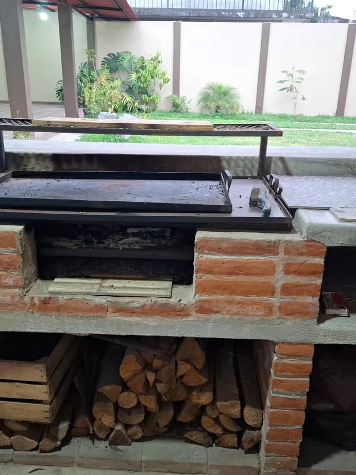 Asador de leña de obra con parrilla, plancha y la leña acomodada abajo